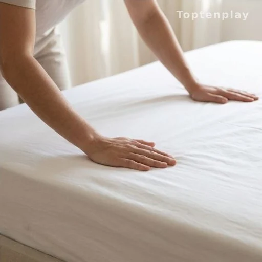 Hands stretching a damp white sheet taut over a mattress